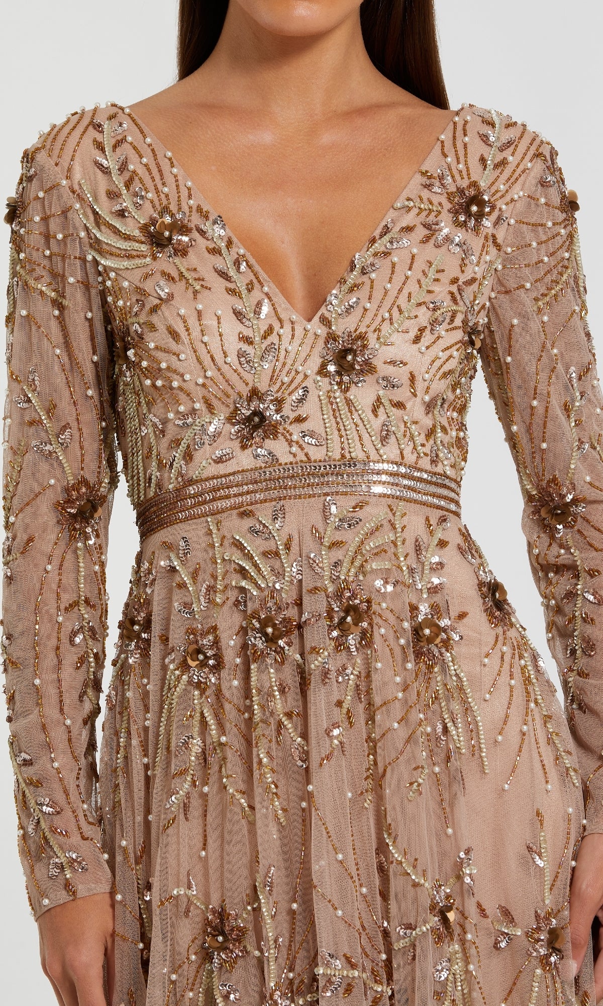 A woman wears the Mac Duggal 6086 Long Sleeve Beaded Formal Gown, featuring gold and bronze beading and sequins in floral and linear designs on nude mesh—a stunning choice for a long beaded formal dress look.